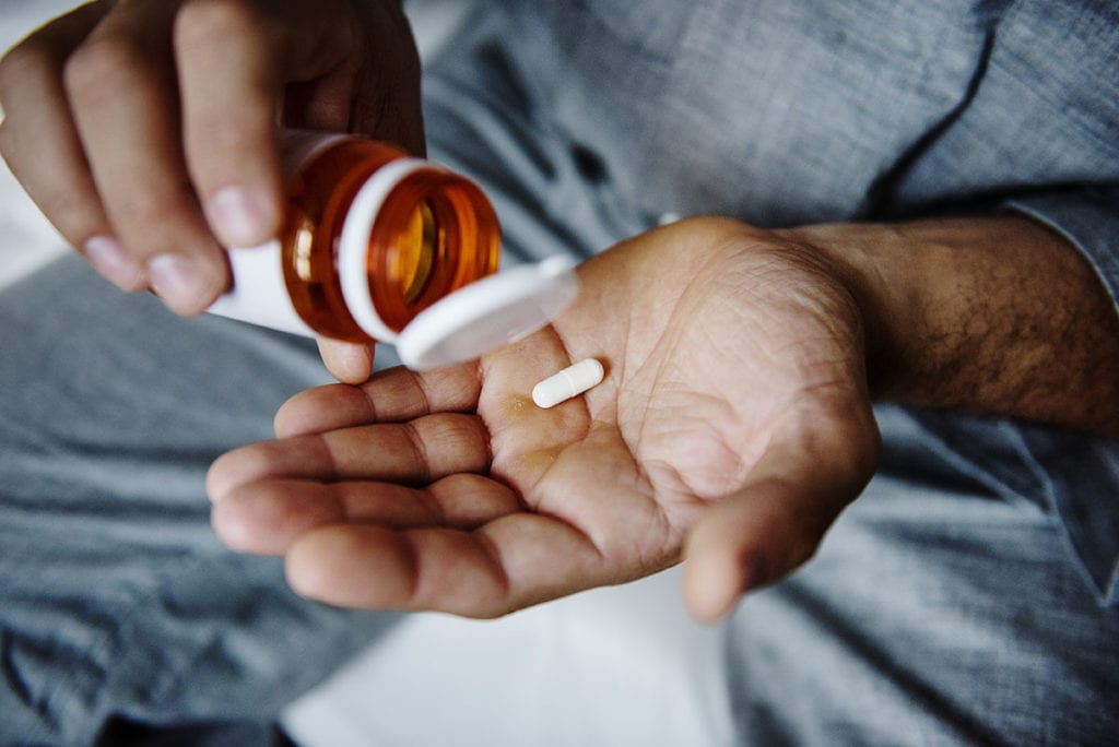 a young man pours a pill into his hand as he thinks about abuse of prescription drugs rising among teens