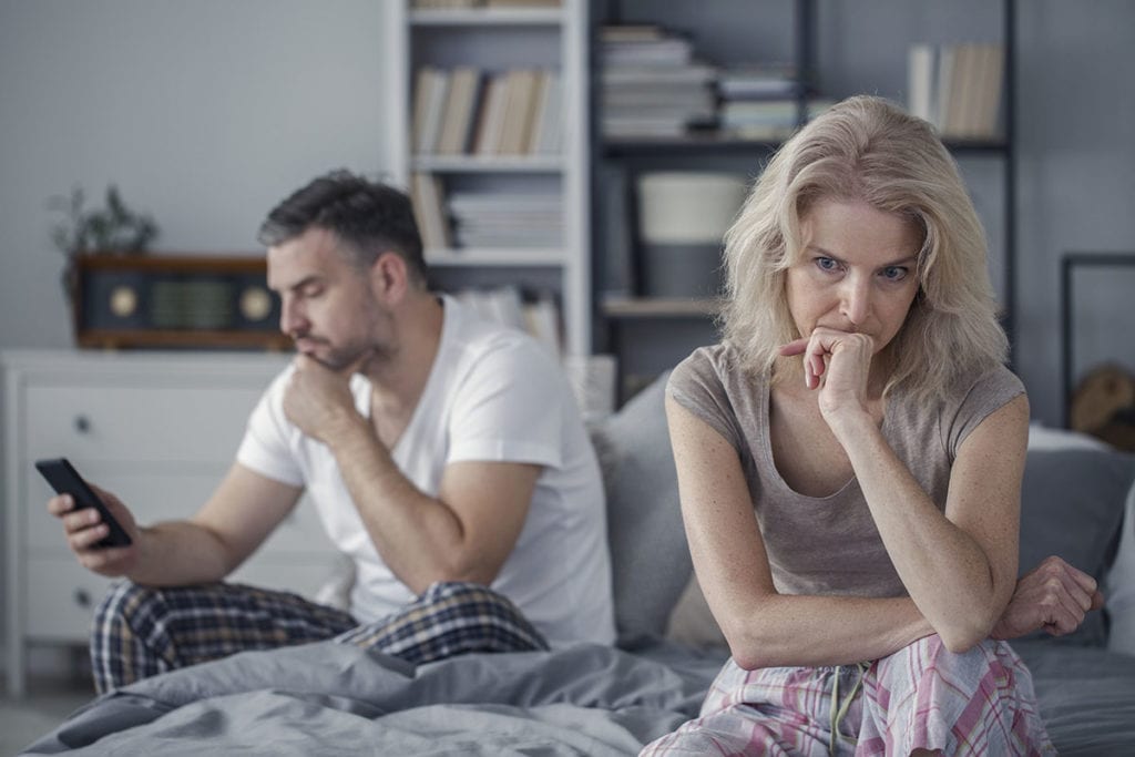 a man researches steroids on his phone as his wife sits in deep thought