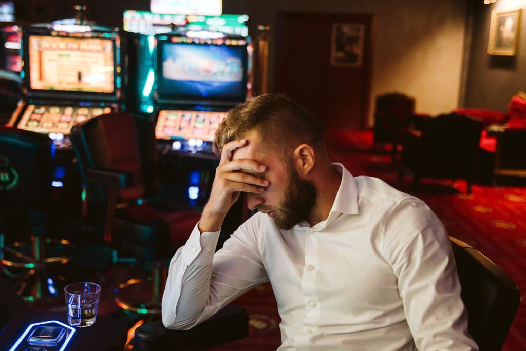 Depressed man drinking at casino while struggling with alcohol and gambling addiction