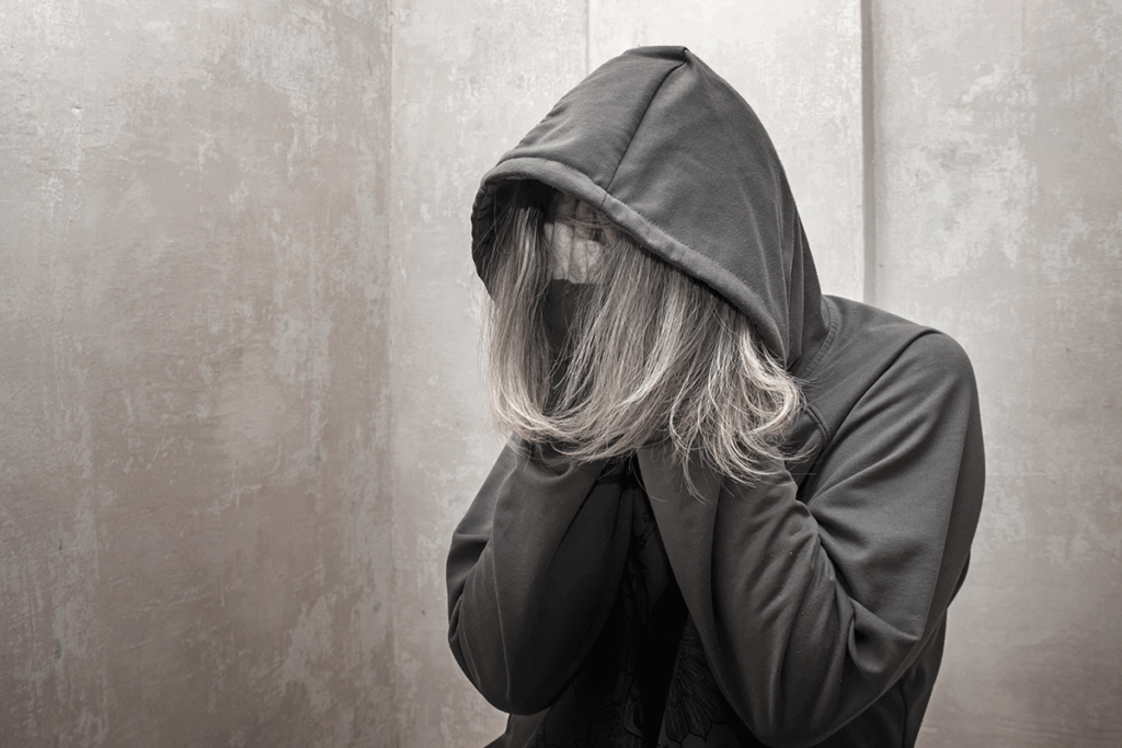 Person in hoodie hiding face with their hands using self-harm as a coping mechanism