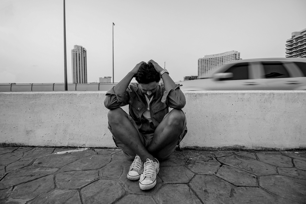Man sitting on side of road with his head in his hands struggling with irritable depression