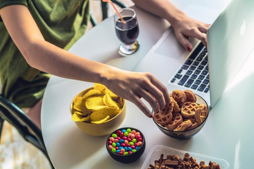 a person snacks on several junk food items while on the computer