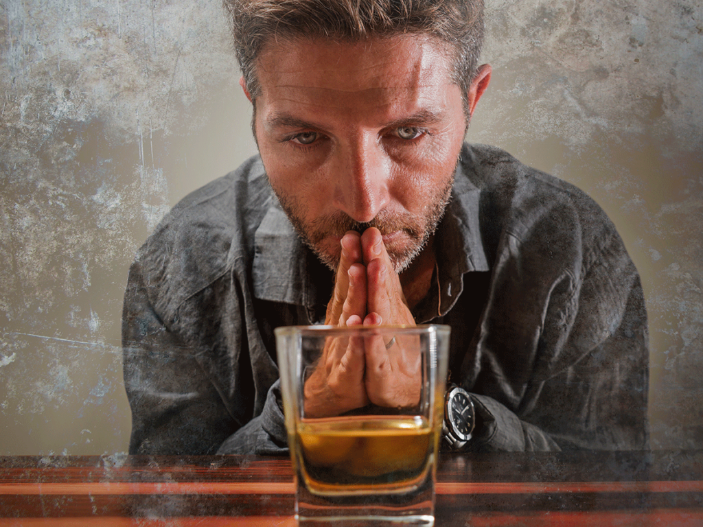 Man looking at glass of liquor before drinking out of boredom