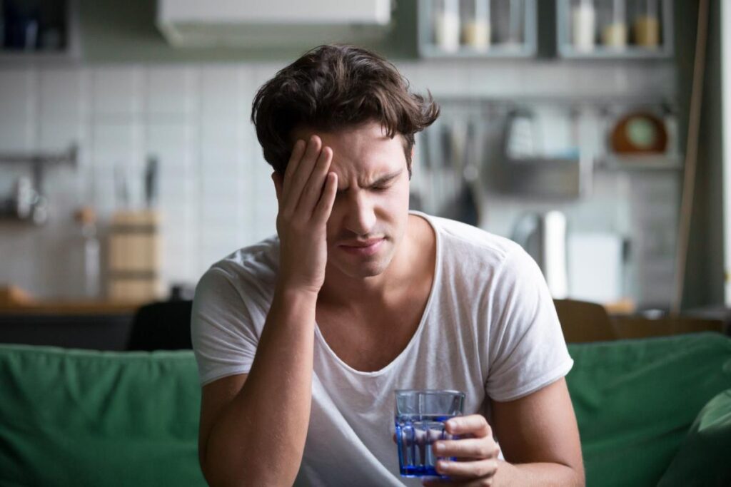 man on couch with drink considering the connection between genetics and hangovers