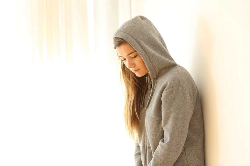 Shy person in hoodie leaning against wall wondering about the differences between introvert vs shy vs social anxiety