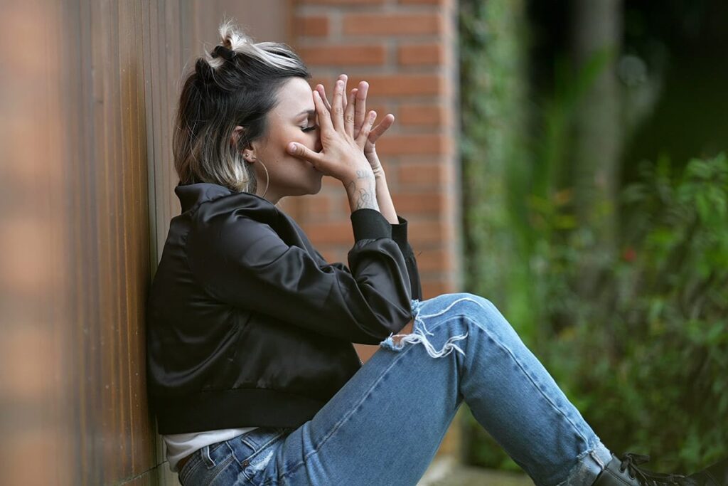 Person sitting against a wall and overcoming the shame of addiction