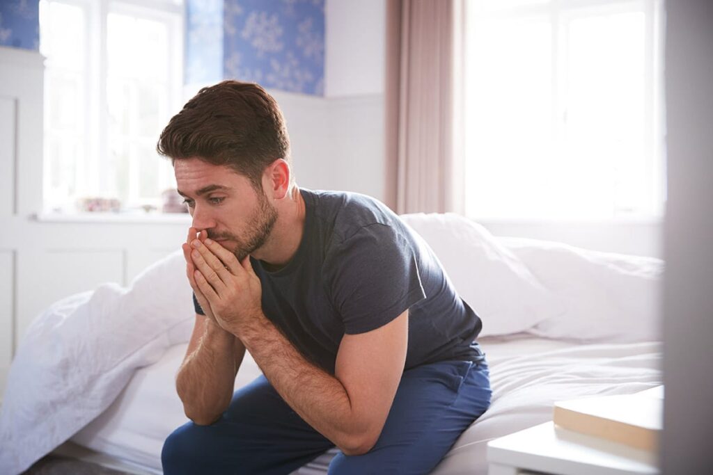 man sitting on edge of bed considers reasons why men keep depression secret