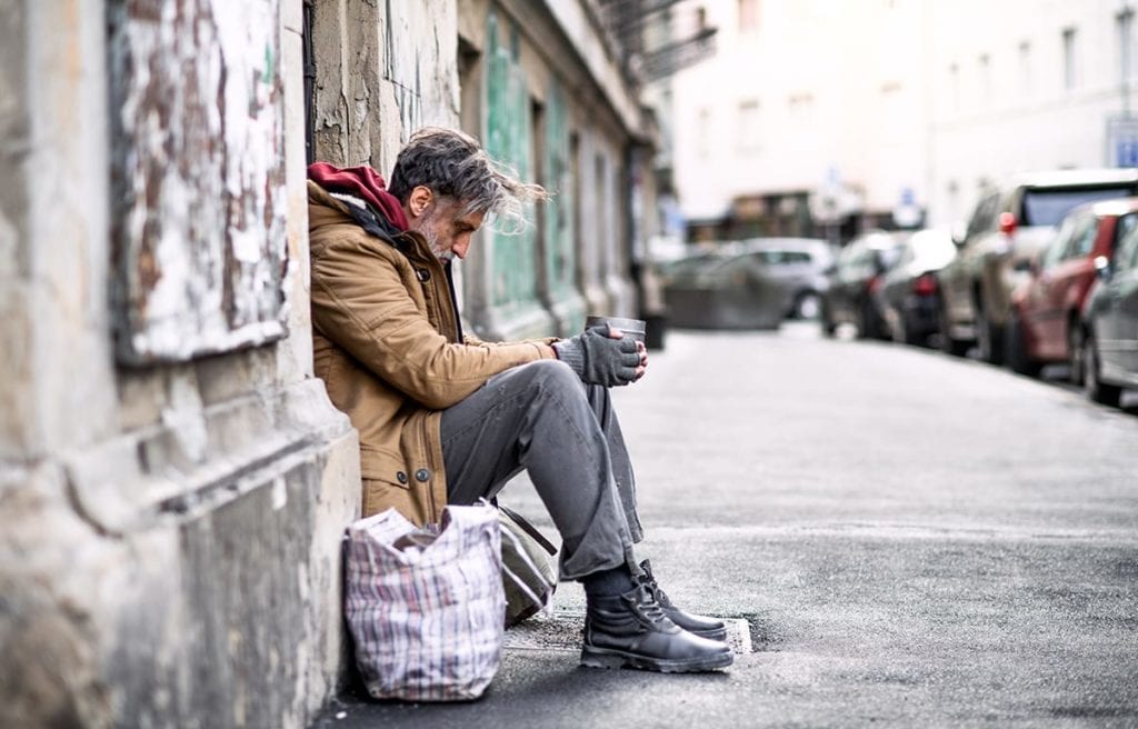 A homeless man sits on a wall and thinks about heroin abuse among the homeless