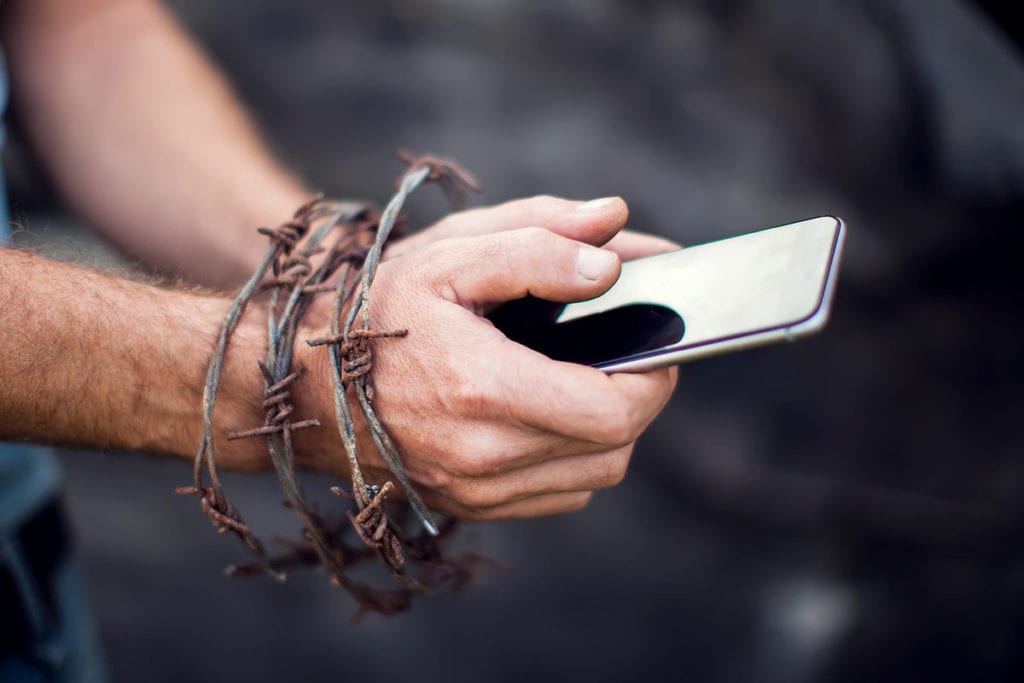 a person stares at his phone as his hands are bound by porn addiction, which lharms teens marriages and real life encounters