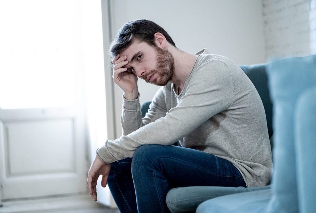 a man sits on his couch holding his head and wonders is mild depression a concern