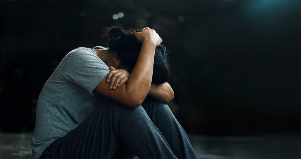 a man sits on the ground and covers his head as he thinks about the causes of complex post traumatic stress disorder