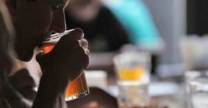 man drinking a glass of alcohol with a bar full of empty glasses in the background and a need for residential alcohol treatment centers