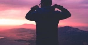 man puts his hood up on mountain at sunset while practicing the daring way