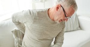 older man on couch holds his back and needs a pain management program