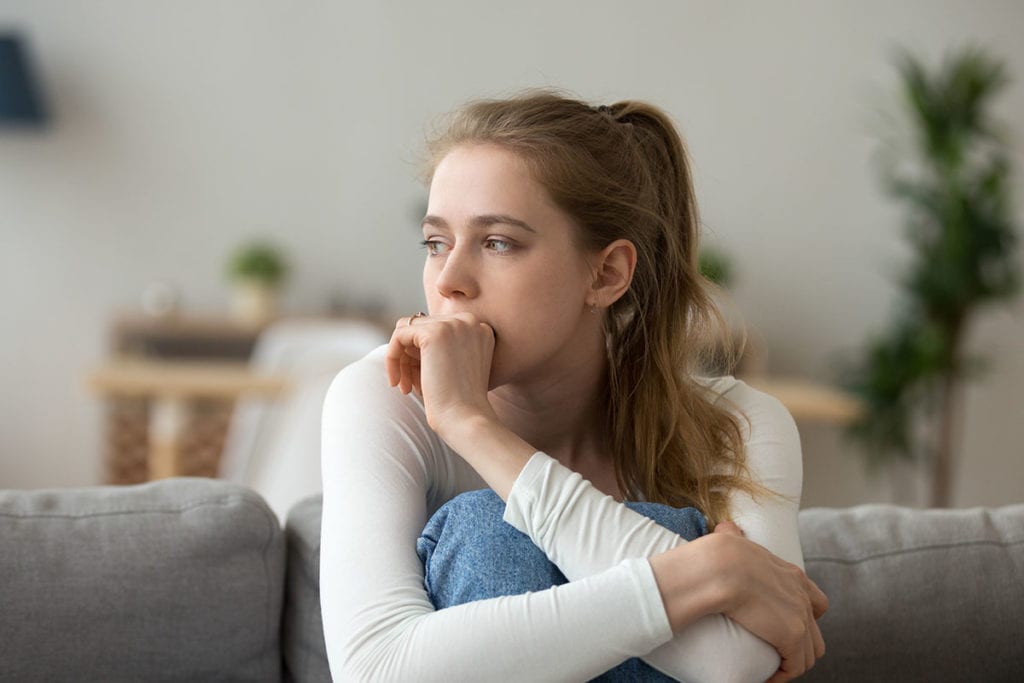 young woman sits on couch with her hand on her mouth wondering to i have a dependent personality disorder