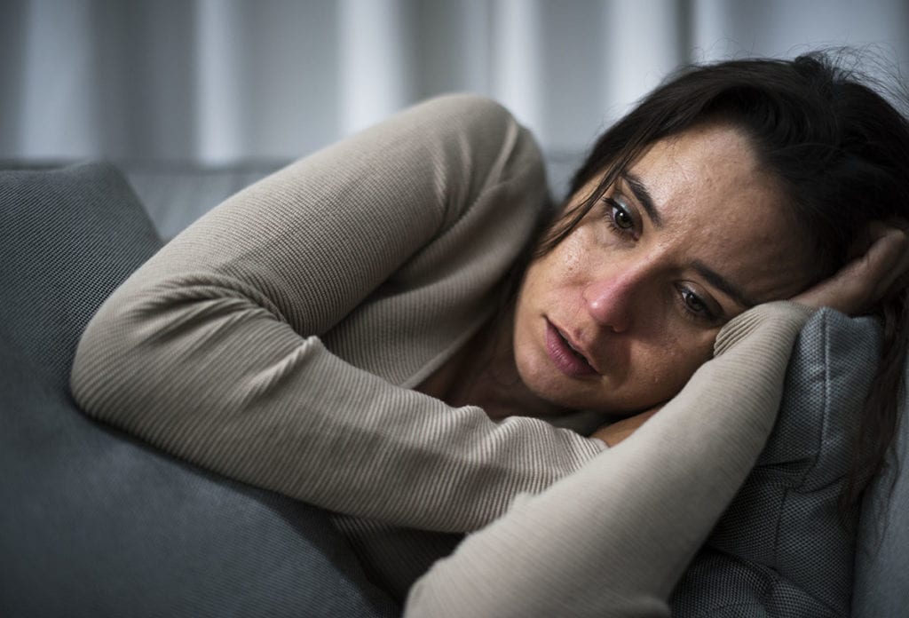 struggling woman lies on couch suffering from heroin withdrawal symptoms