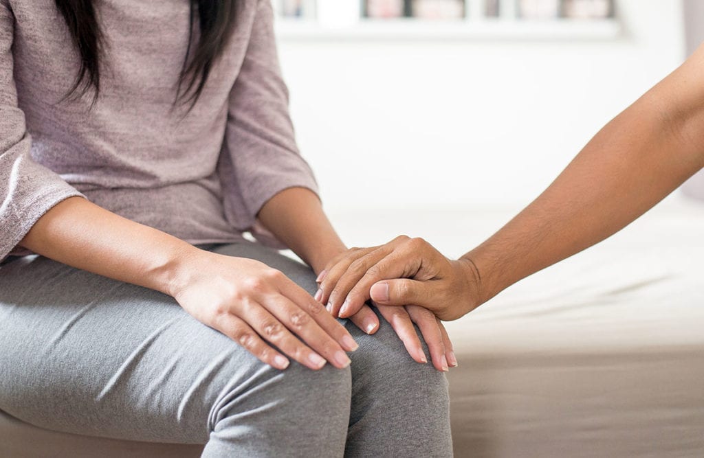 hand reassuring woman sitting on bed as she chooses to go to a substance abuse counselor