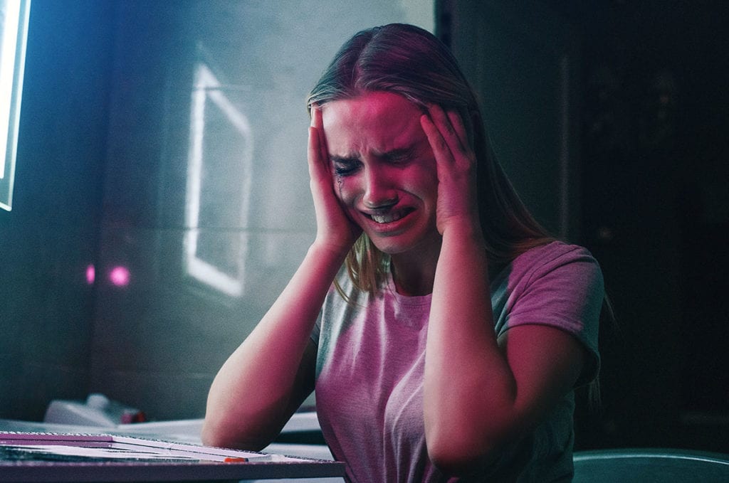 crying girl sits in dark with her hands on her head needing tips for living with ptsd