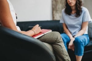 female patient sits on couch while talking to a therapist with notebook in a benzo addiction treatment center