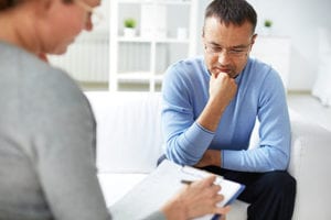 female therapist takes notes on a clipboard while male patient thinks in a life skills training program