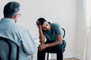 male sits in a chair with his head in his hand while talking to a therapist in a codeine addiction treatment center