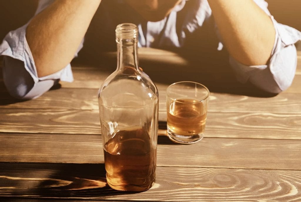 man distressed with bottle and glass of alcohol thinking what are the signs of a drinking problem
