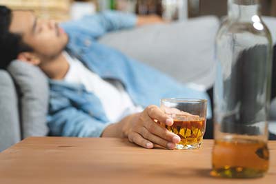 man drinking on couch in need of promises behavioral health mens alcohol rehab center