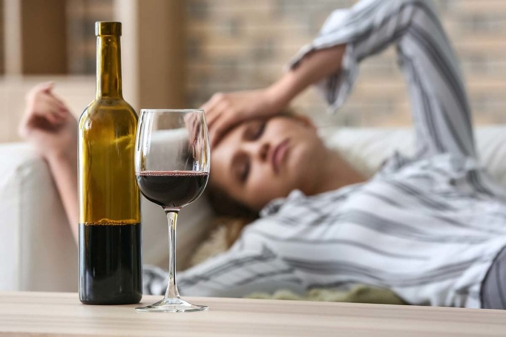 alcoholic woman laying down dealing with the physical effects of alcohol; she has been drinking