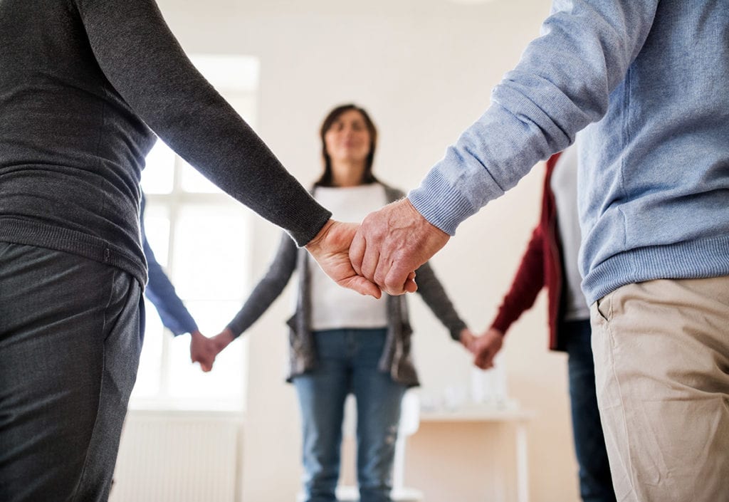 a group of people hold hands as they discuss the features of a good alcohol addiction treatment center