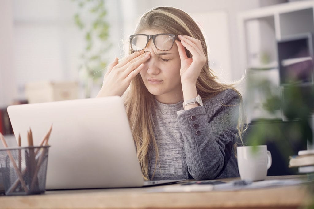 a woman rubs her eyes as she researches signs of a drug and alcohol dependence on a laptop