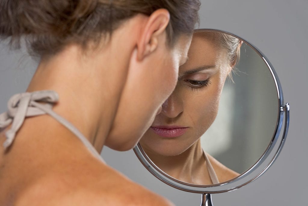 a woman looks into a mirror and wonders why do people binge drink