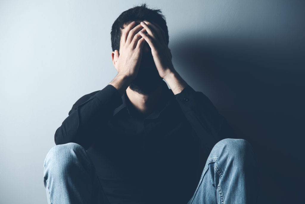 a man covers his face as he thinks about mental disorders from drug use