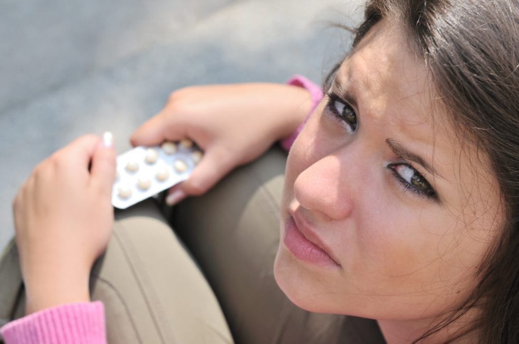 a young woman looks up as she holds pills and thinks about statistics on teen substance abuse