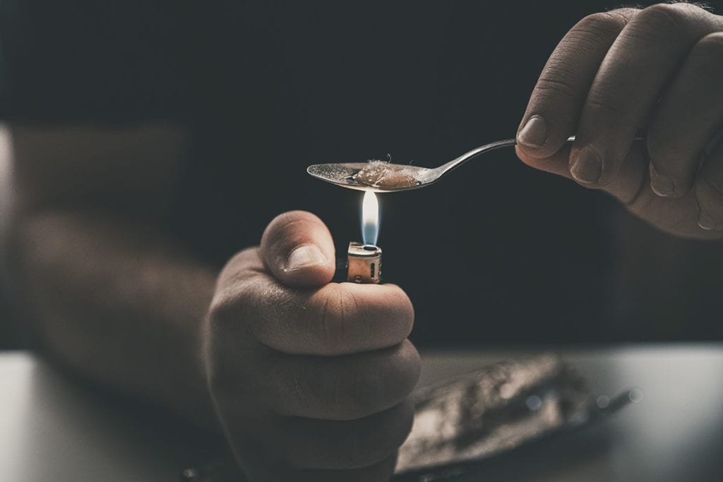 a person holds heroin spoon and wonders about the history of heroin use