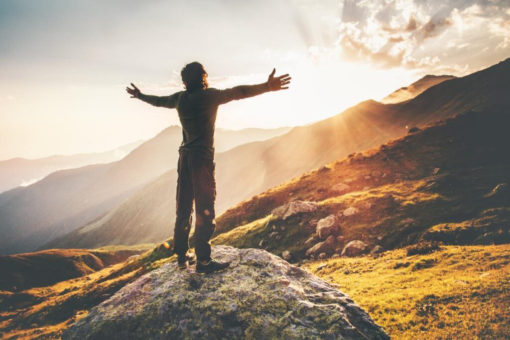 a man stands triumphantly on a cliff at sunrise