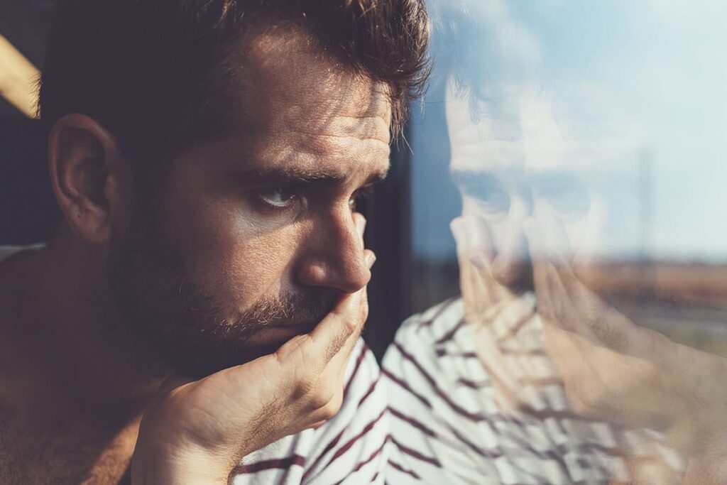 Man looks out window in distress as he struggles with PTSD and substance abuse