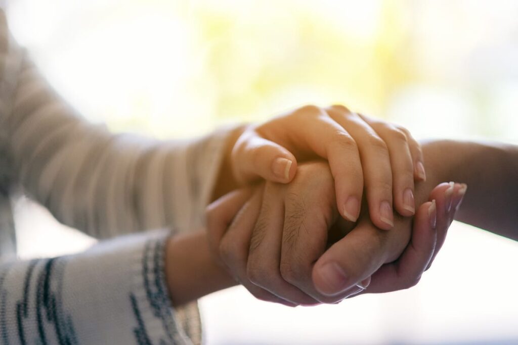Person holds hands with a loved one as they learn the difference between helping vs. enabling