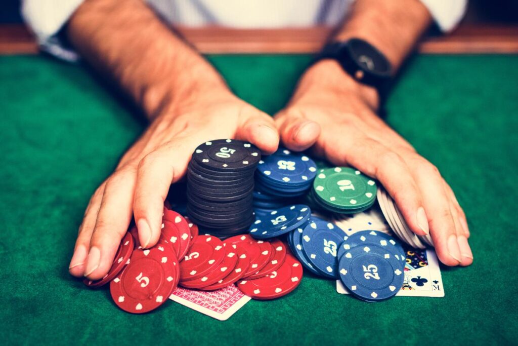 A person's hand gathering poker chips while experiencing one of the stages of compulsive gambling