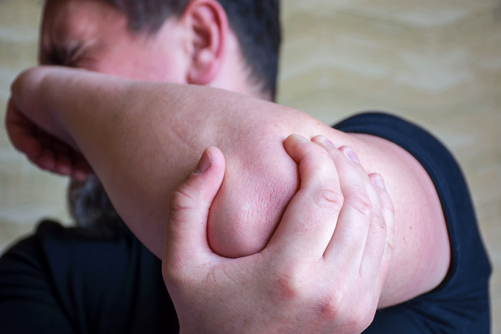 Man holding elbow and experiencing uncomfortable signs of alcoholic neuropathy