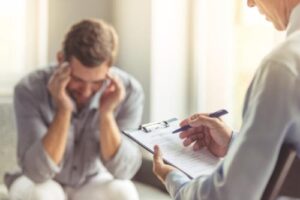 man puts head in hands and considers a men's addiction treatment center