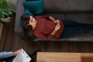 woman sitting on couch considers a women's addiction treatment center